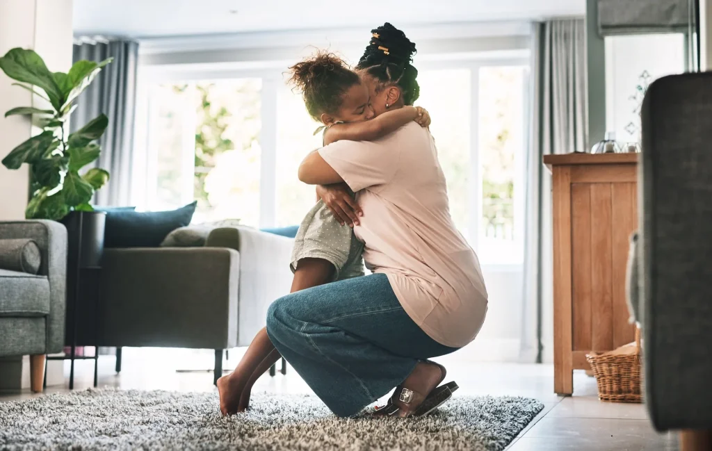 Parent hugging a child in a bright living room with large windows